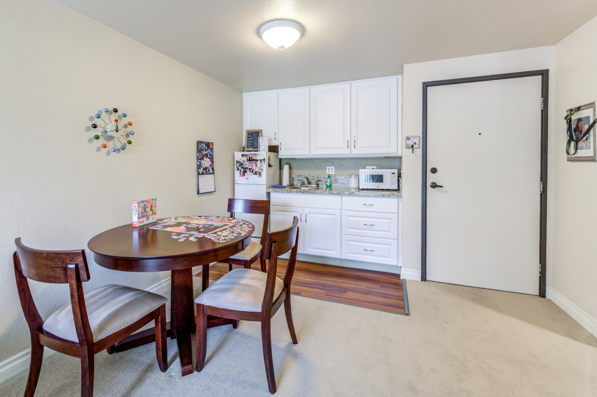 A compact dining and kitchen area with a wooden table, chairs, white cabinets, and essential appliances.
