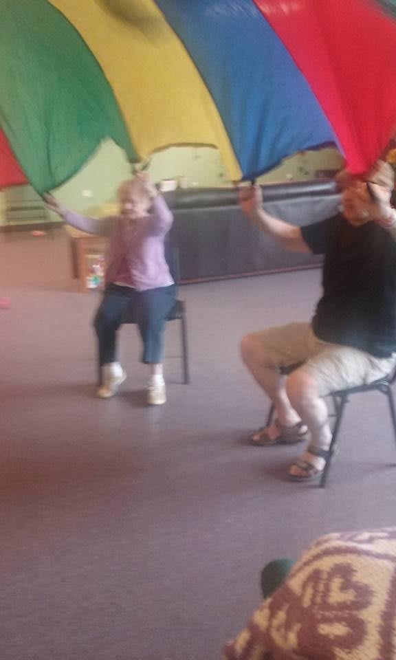 Children and adults participating in an indoor activity with a colorful parachute.