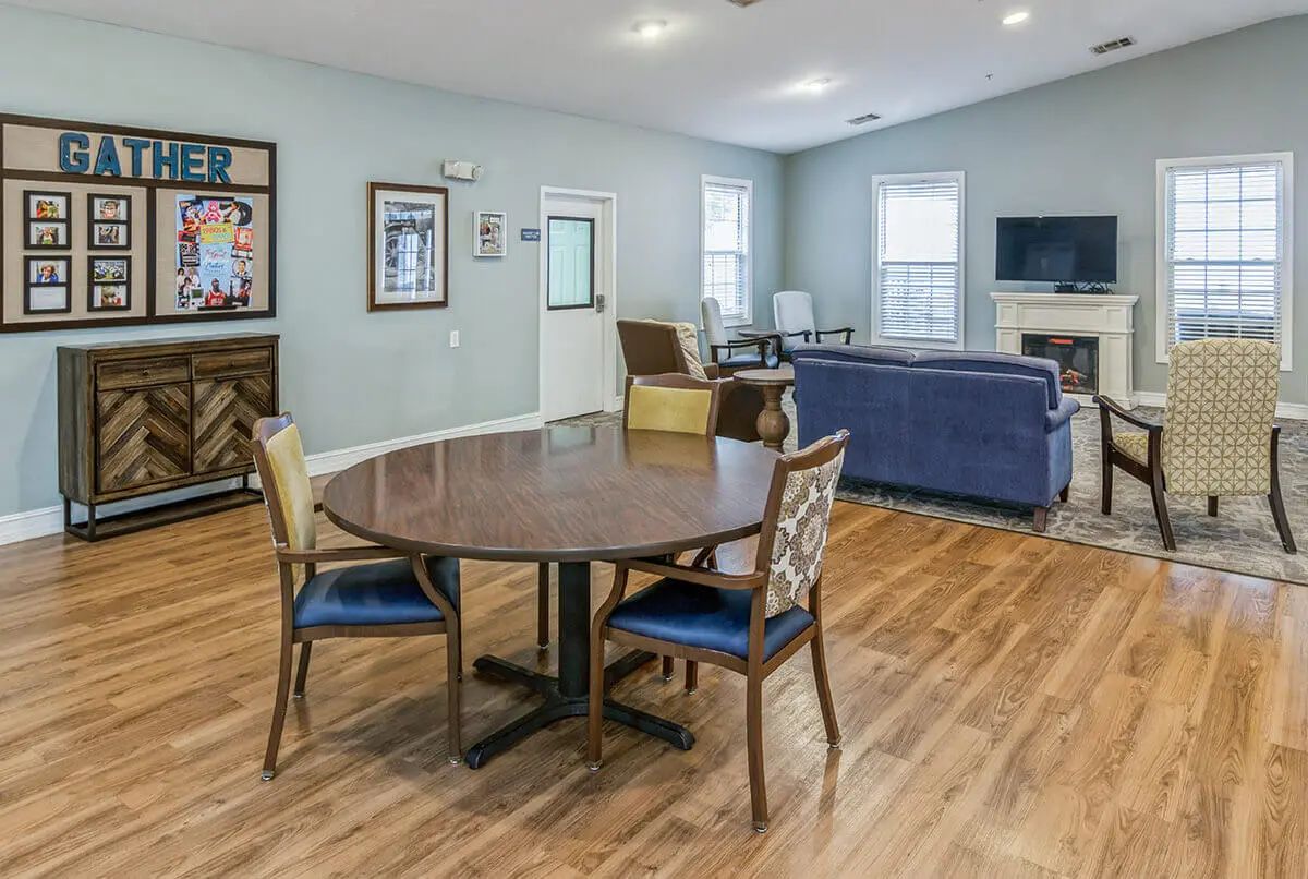 A spacious living room with wood flooring featuring a round table and chairs, a sofa set, and a fireplace.