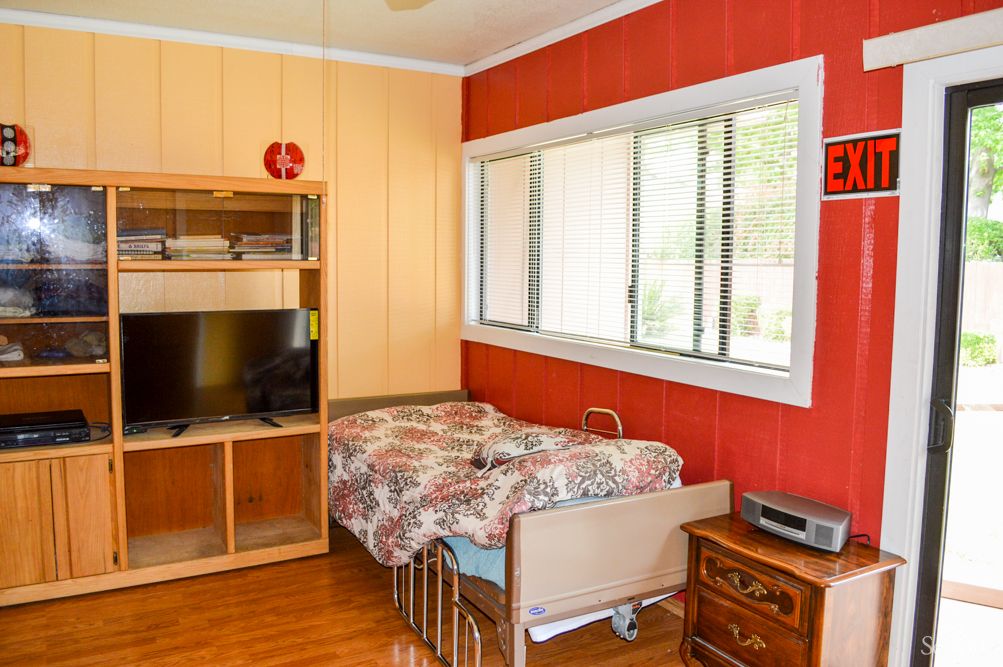 A cozy bedroom featuring a single bed, wooden flooring, and a shelving unit with a television.