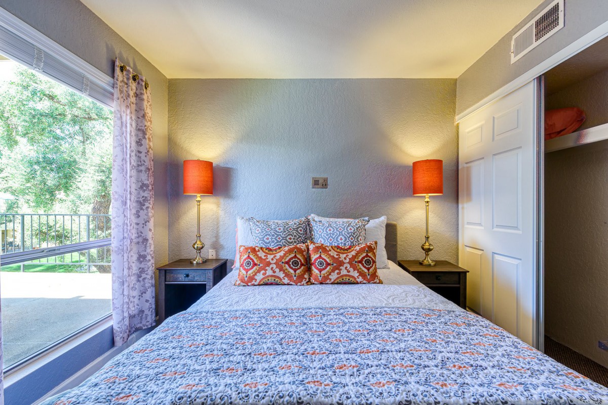 A cozy bedroom with a neatly made bed, flanked by two side tables and orange lamps.
