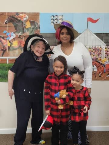 A group of people, including two children in plaid outfits and two adults wearing hats, pose indoors.
