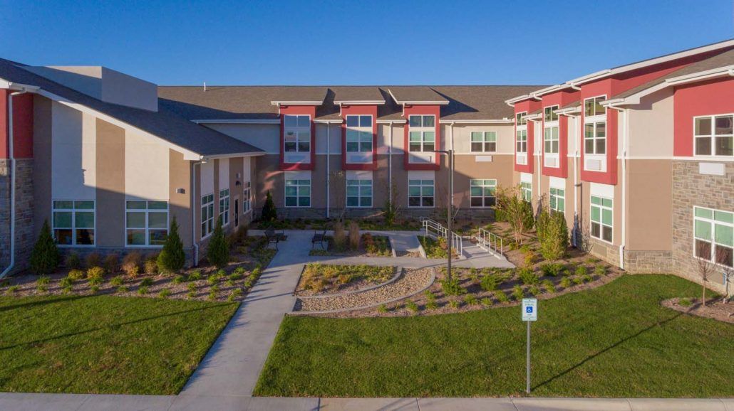 A modern residential apartment building with landscaped grounds and a clear blue sky.