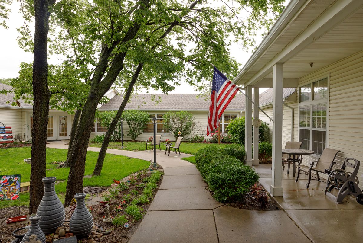 A peaceful garden pathway with lush greenery and an American flag displayed on the porch.