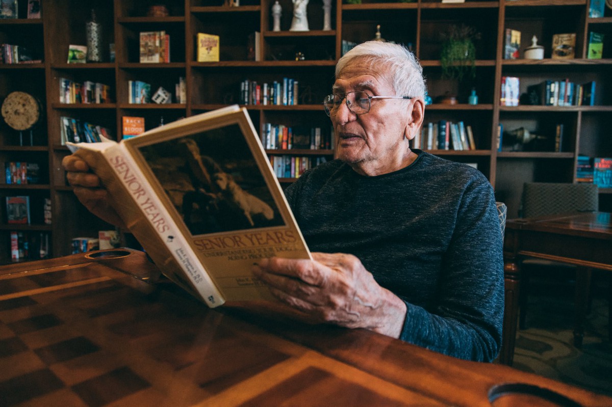 A senior man enjoys reading a book in a cozy library.