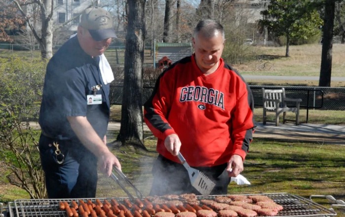 Two individuals grilling food outdoors in a park setting.