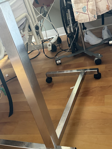 A close-up view of a wheeled support frame, likely part of medical equipment, on a wooden floor.