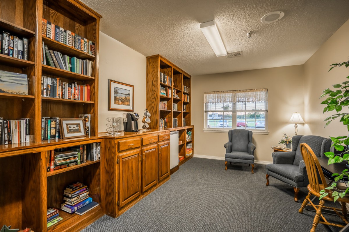 A cozy library room with wooden bookshelves, two armchairs, and a window.
