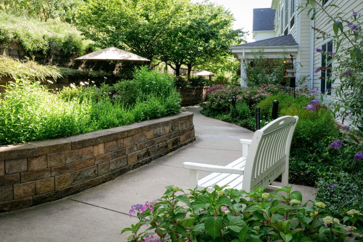 A serene garden with a winding pathway, surrounded by lush greenery and outdoor seating.