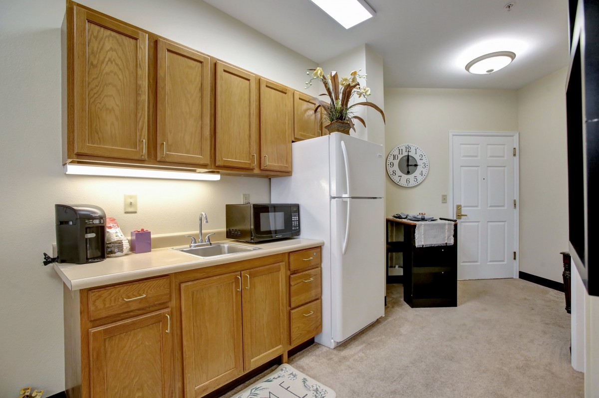 A tidy kitchen with wooden cabinets, a refrigerator, and a microwave on the countertop.