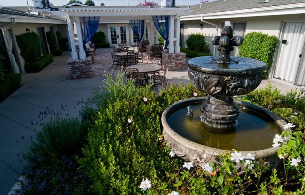 A serene garden patio with a central fountain, lush greenery, and comfortable outdoor seating.
