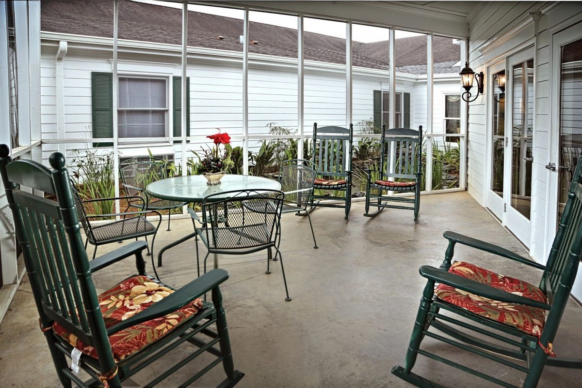 A cozy screened porch with rocking chairs and a glass table, adorned with potted flowers.