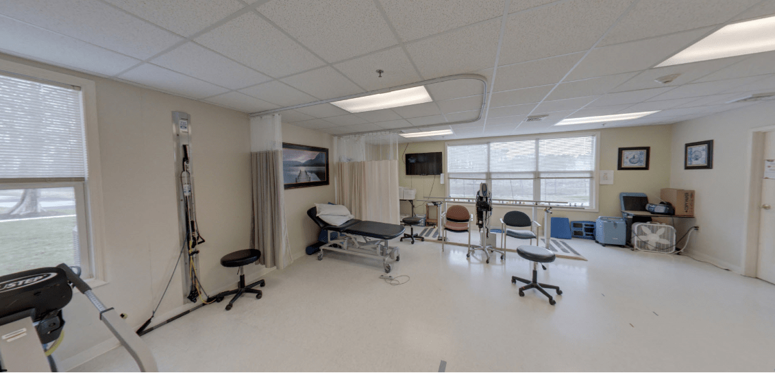 A medical treatment room with an examination table and several chairs.