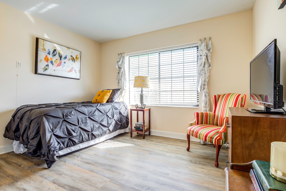 A cozy bedroom with a single bed, striped chair, and a window letting in natural light.