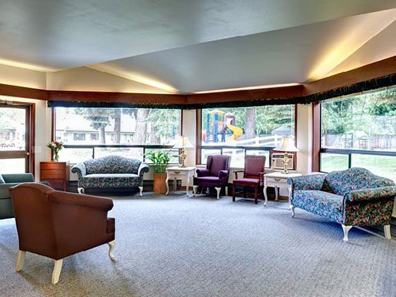 A spacious and well-lit living room with comfortable sofas and chairs, surrounded by large windows.