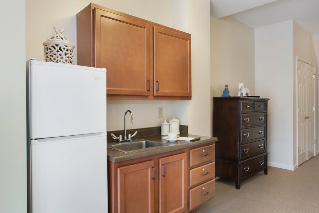 A small kitchenette with wooden cabinets, a white refrigerator, and a sink area.