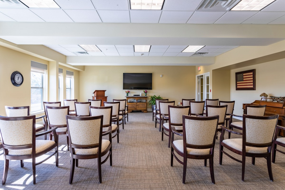 A well-lit conference room with arranged chairs facing a television and podium.