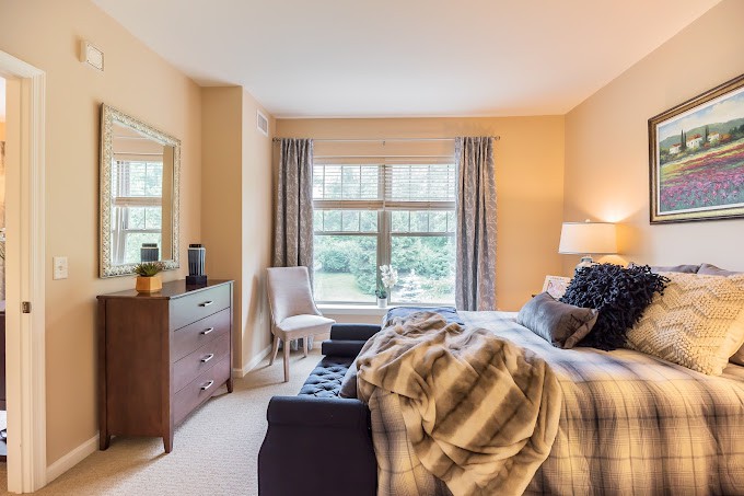 A cozy bedroom with a neatly made bed, dresser, and large window with curtains.