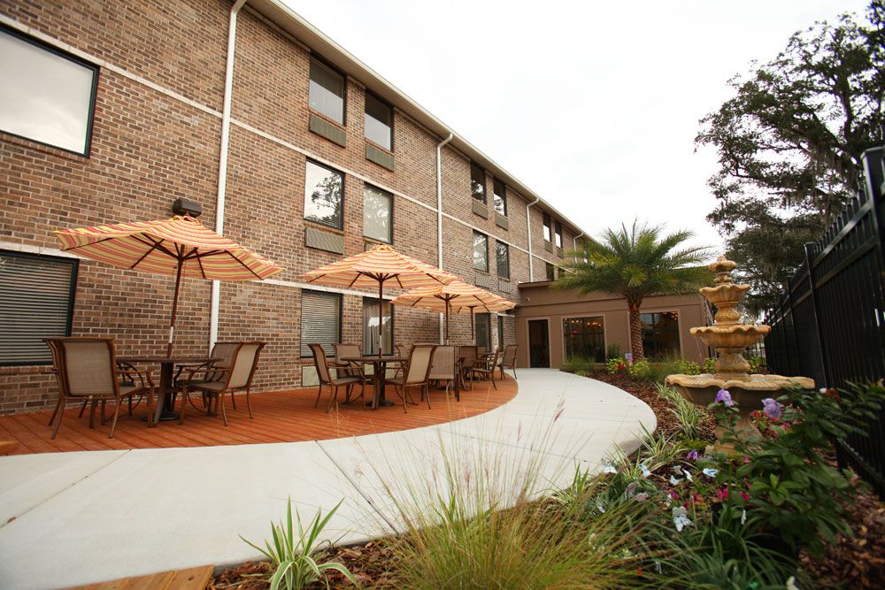 A brick building with outdoor seating and umbrellas, surrounded by landscaped gardens and a fountain.