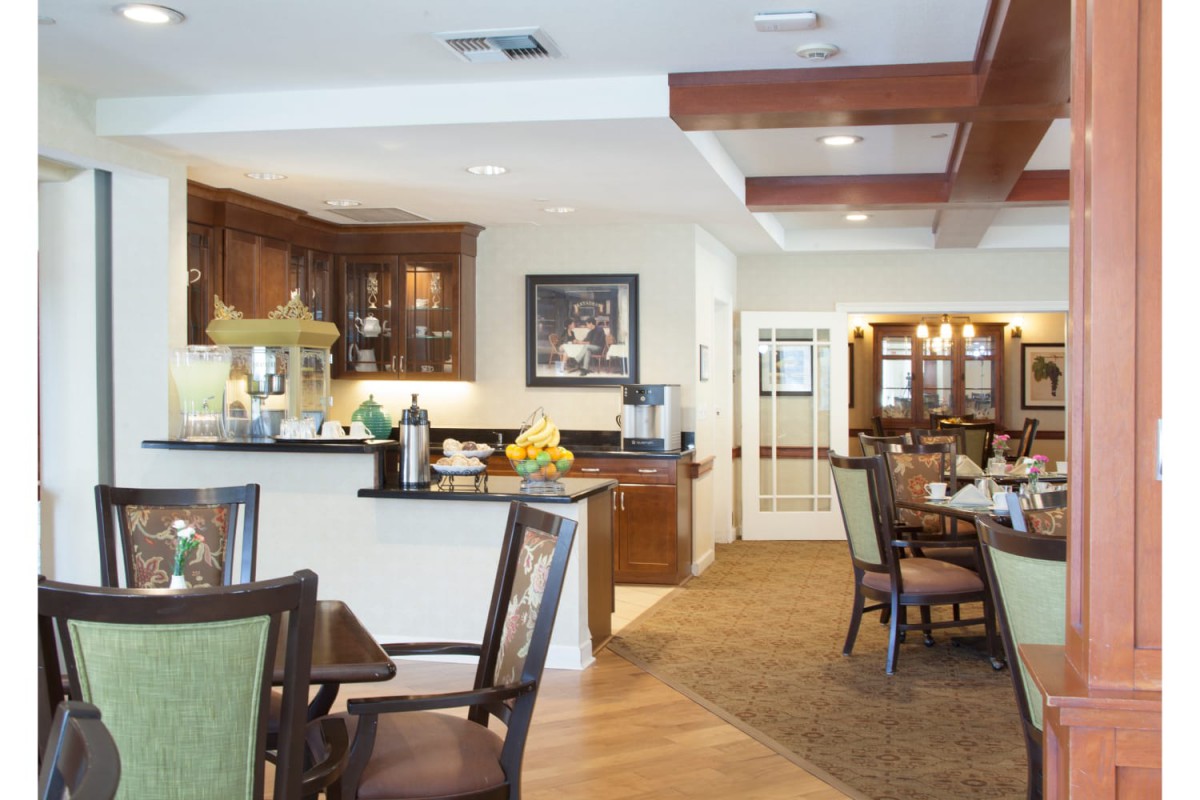 A cozy dining area with wooden floors, a kitchen counter, and several tables and chairs.