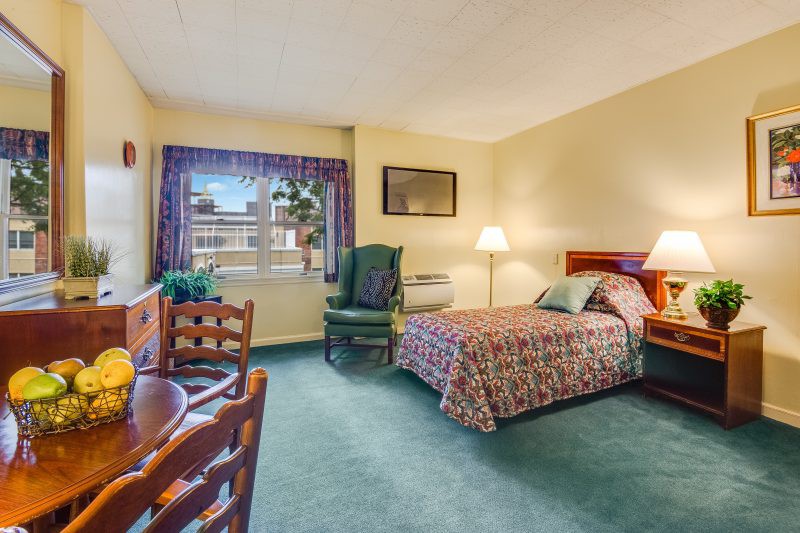 A cozy hotel room featuring a bed, chair, table, and a window with curtains.