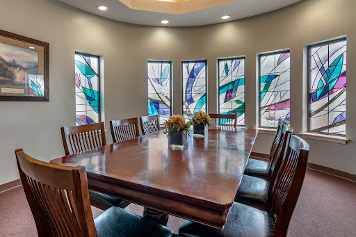 A stylish dining room featuring a large wooden table surrounded by chairs, illuminated by beautiful stained glass windows.