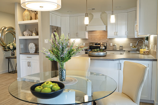 A beautifully designed modern kitchen and dining area with a glass table, fresh flowers, and a bowl of green apples.
