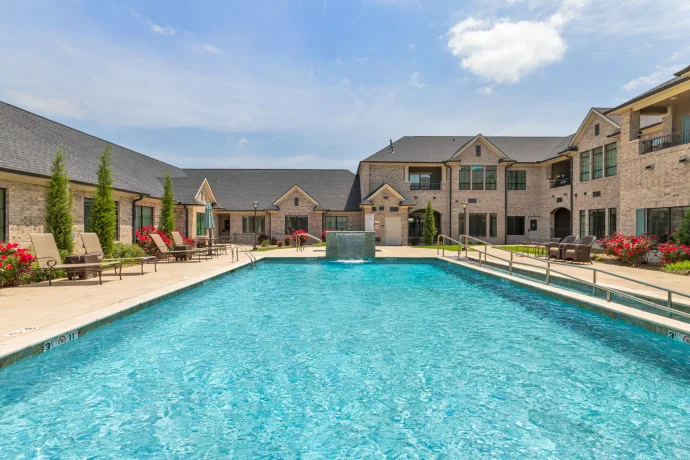 A modern residential complex featuring a large outdoor swimming pool under a clear blue sky.