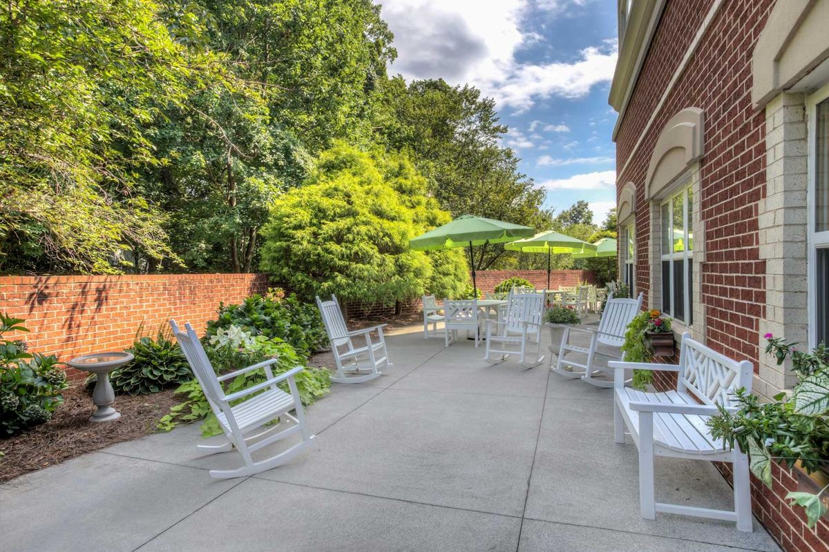 A sunny outdoor patio with rocking chairs and umbrellas, surrounded by lush greenery.