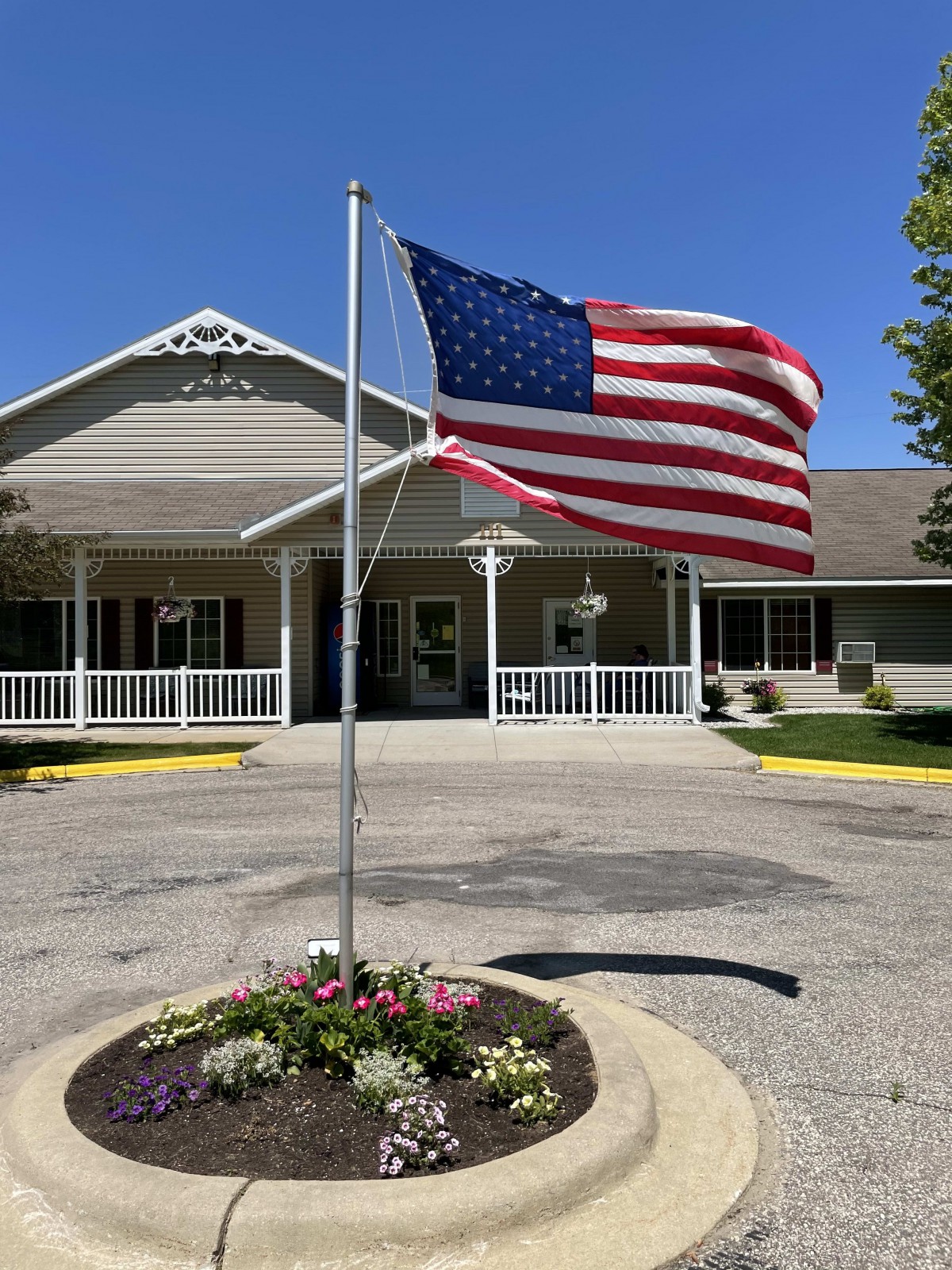 An American flag waves proudly in front of a building with a flower bed and inviting entrance.