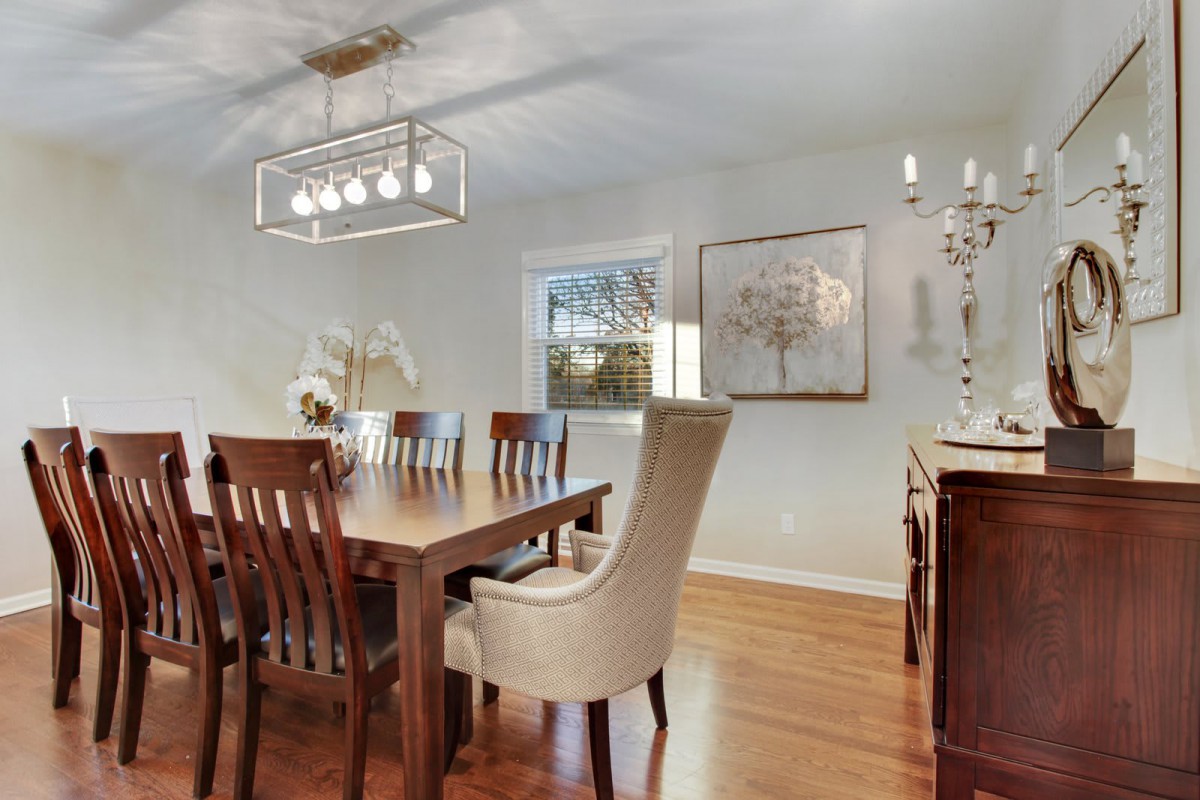 A modern dining room with a wooden table and chairs, featuring elegant lighting and wall art.