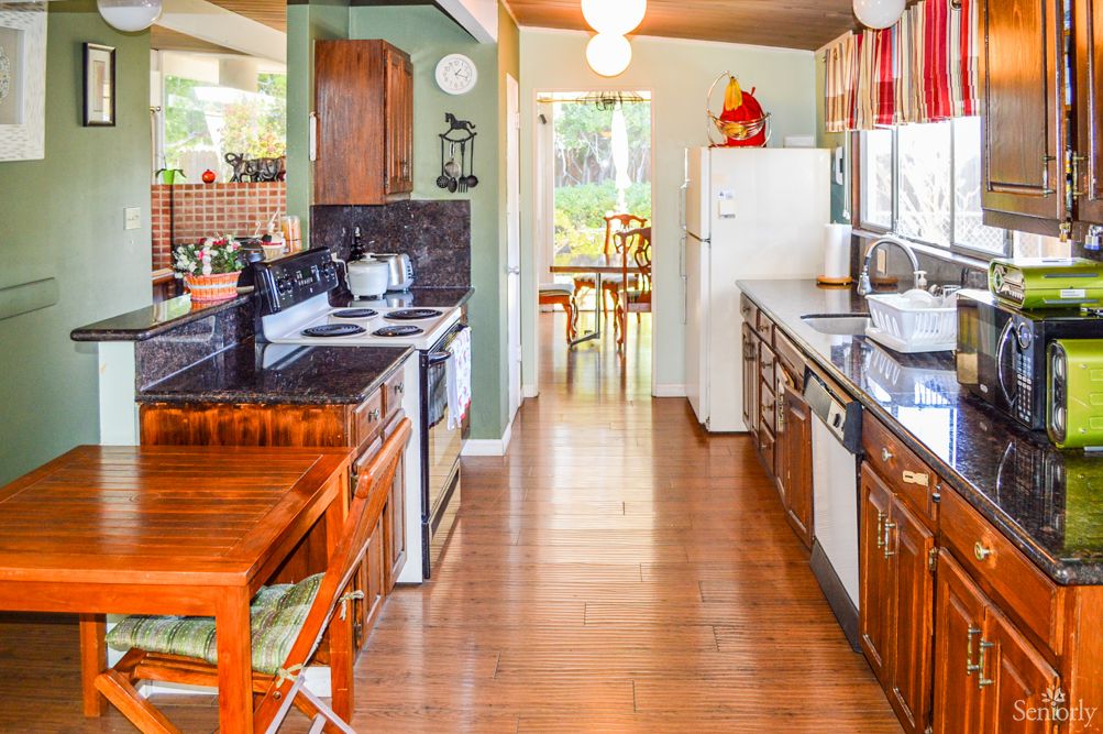 A cozy kitchen featuring wooden cabinets, appliances, and a dining area in the background.