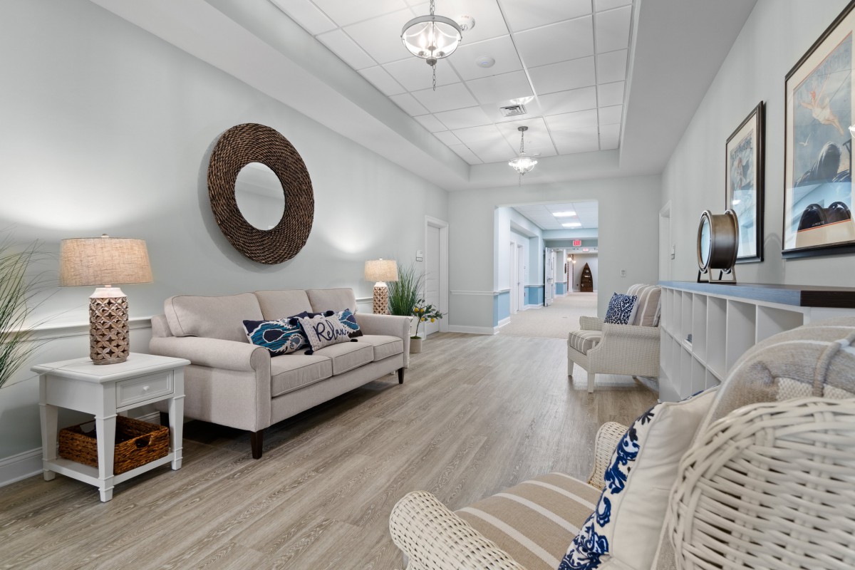 A modern living room with neutral tones and elegant decor, featuring a sofa, mirror, and chandeliers.