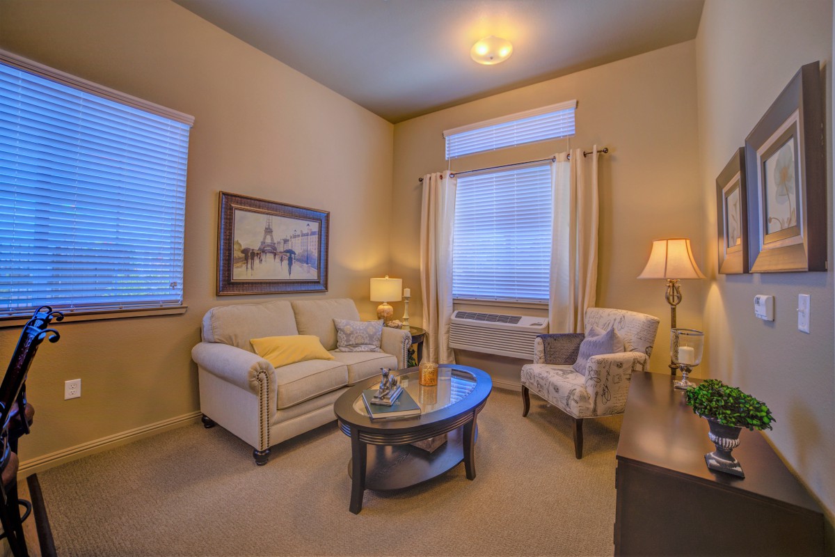 A cozy living room with a sofa, armchair, and coffee table, warmly lit by lamps.