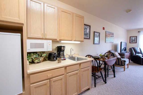 A cozy kitchenette area with wooden cabinets, a countertop featuring a microwave and coffee maker, and an adjacent dining table with chairs.