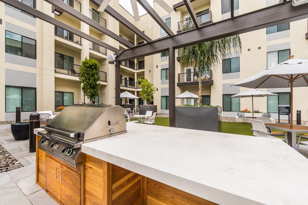 Modern apartment complex patio with a barbecue grill and outdoor seating.