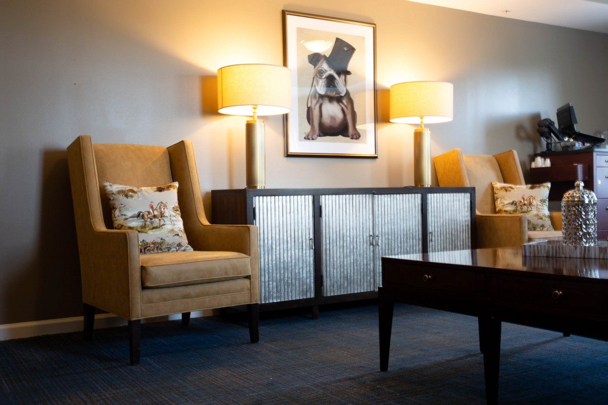 A cozy living room with armchairs, lamps, and artwork above a cabinet.