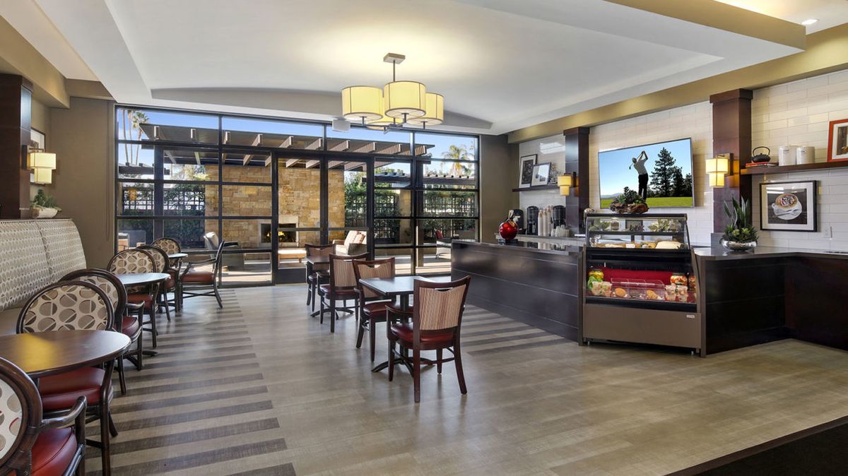 A modern cafe interior with tables, chairs, and a service counter, featuring large windows for natural lighting.