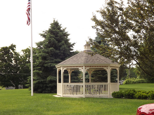 A charming gazebo surrounded by lush greenery and a flag in the background.
