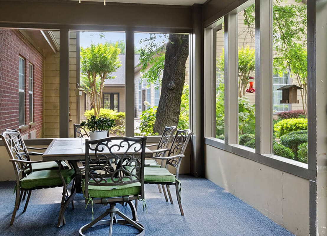 A sunlit dining area with large windows overlooking a garden.