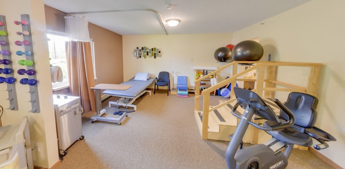 A rehabilitation room equipped with a treatment table, exercise equipment, and exercise balls.
