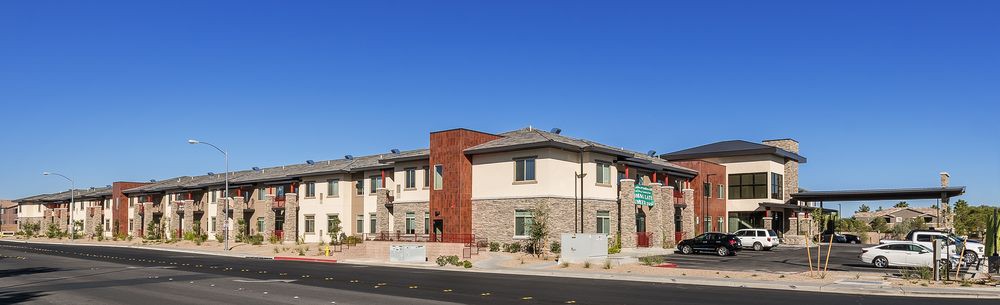 A modern two-story apartment complex situated in an urban residential area under a clear blue sky.