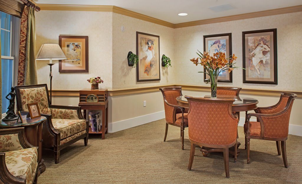 A cozy seating area with a table, chairs, and decorative elements like paintings and a floral arrangement.