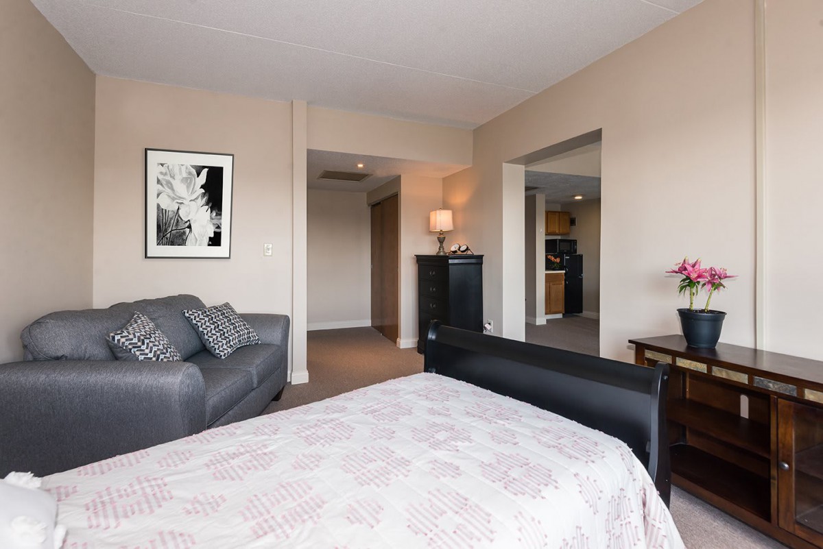 A spacious bedroom with a sofa, bed, lamp, and artwork.
