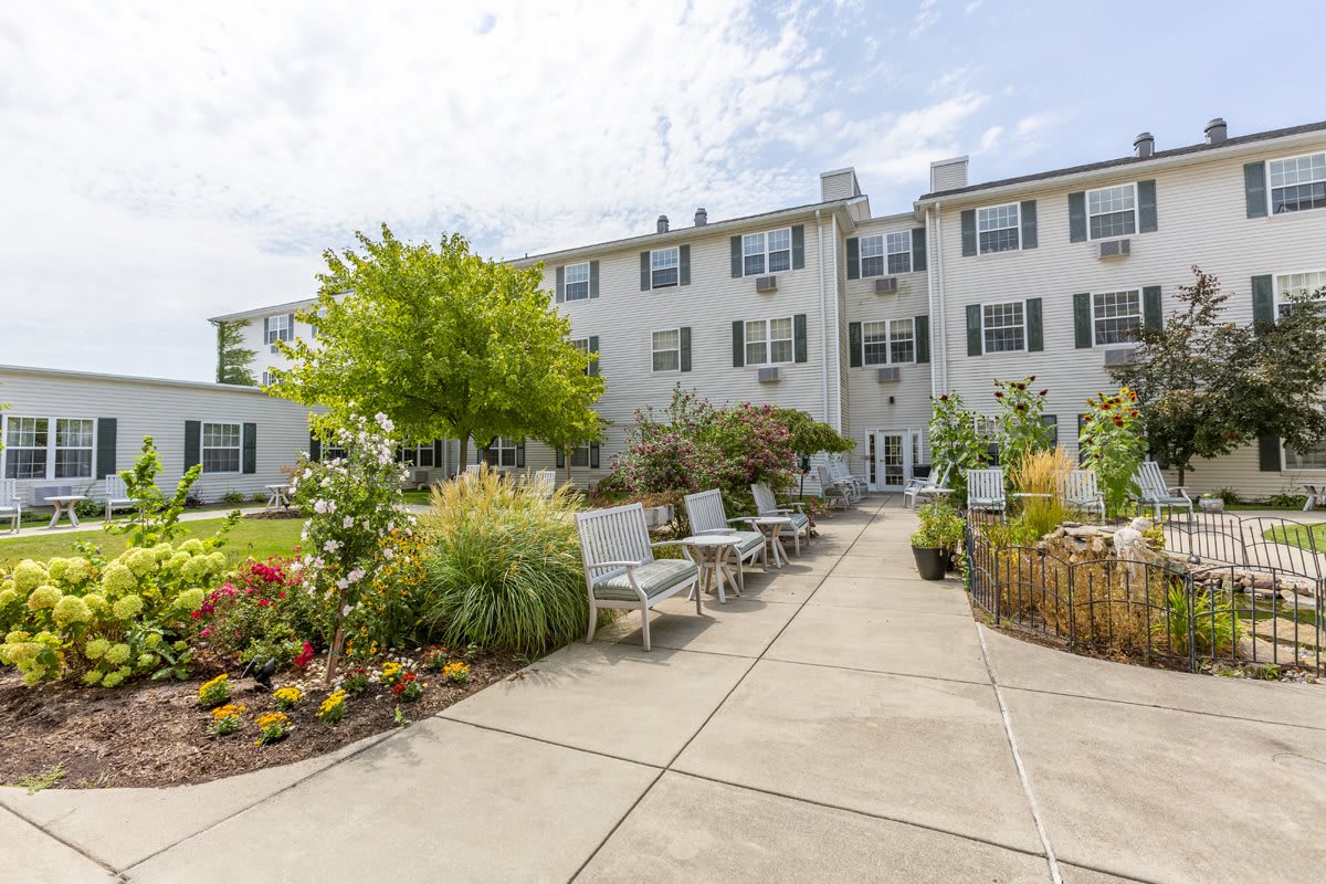A serene outdoor patio area with chairs and vibrant flower gardens in front of a white apartment building.