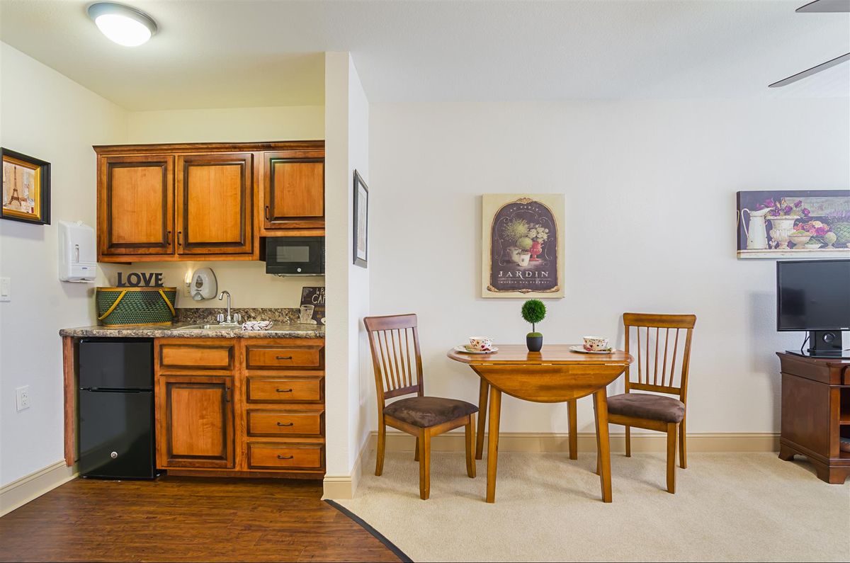 A cozy dining area with a small wooden table and chairs adjacent to an open kitchen featuring wooden cabinets.