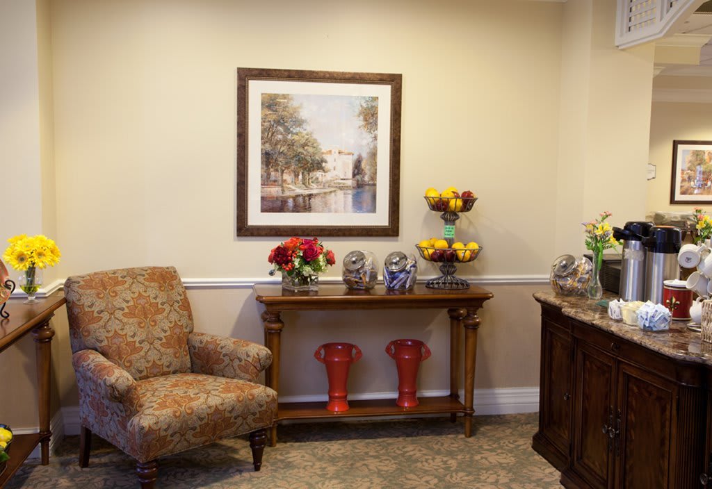A cozy reception area featuring an armchair, a console table adorned with flowers and decorative items, and a framed painting on the wall.