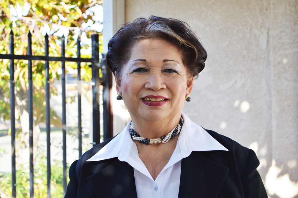 A woman in formal attire standing outdoors and smiling.