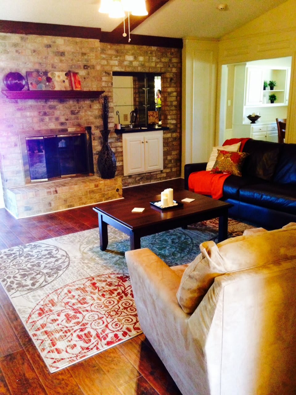 A cozy living room with a brick fireplace, comfortable seating, and a colorful decorative rug.