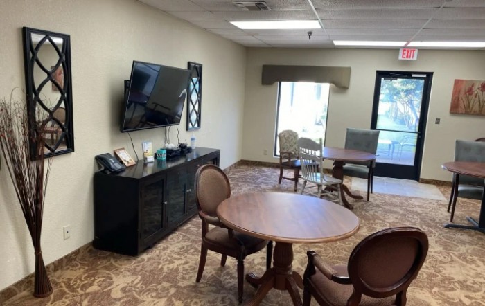 A cozy living room with a television, round tables, and chairs on a carpeted floor.